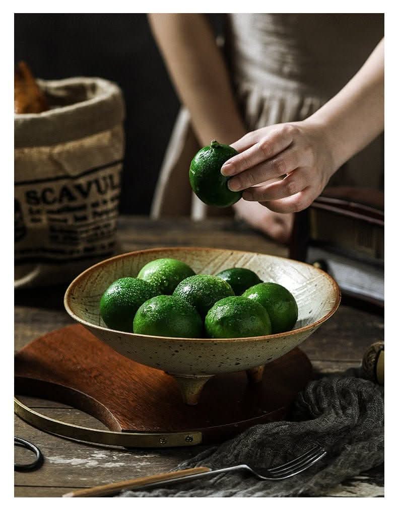 Tripod Stoneware Fruit Plate holds glistening green limes, a rustic home decor piece.